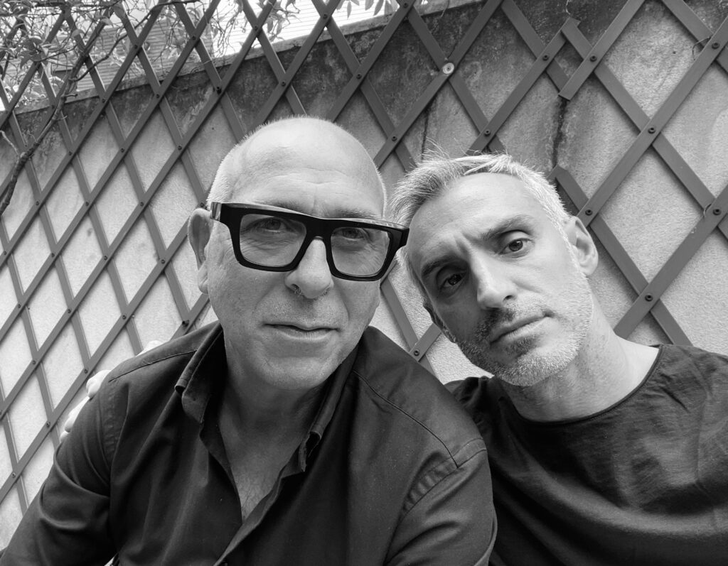Selfie of two men under a wooden trellis